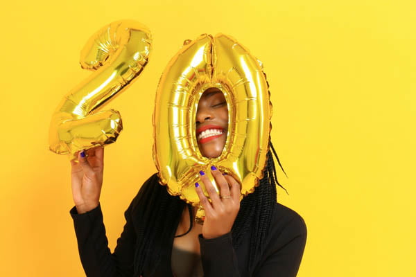 Best Devotionals for 20 Somethings - lady holding balloons of 20 over her face