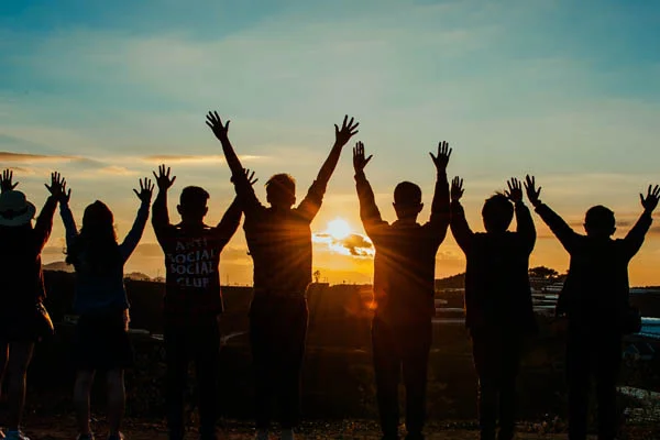 Best Devotionals for 20 Somethings -  Group of people with arms raised at sunset