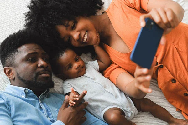 Best Devotionals for 20 Somethings - couple with infant taking family selfie on bed